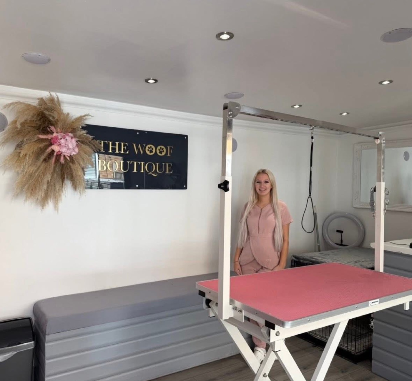 Inside The Woof Boutique garden salon: pink grooming table, gold and black sign and pampas grass